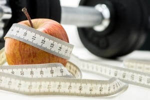 Closeup of apple wrapped with measuring tape and weights in background. Conceptual of fitness and dieting.